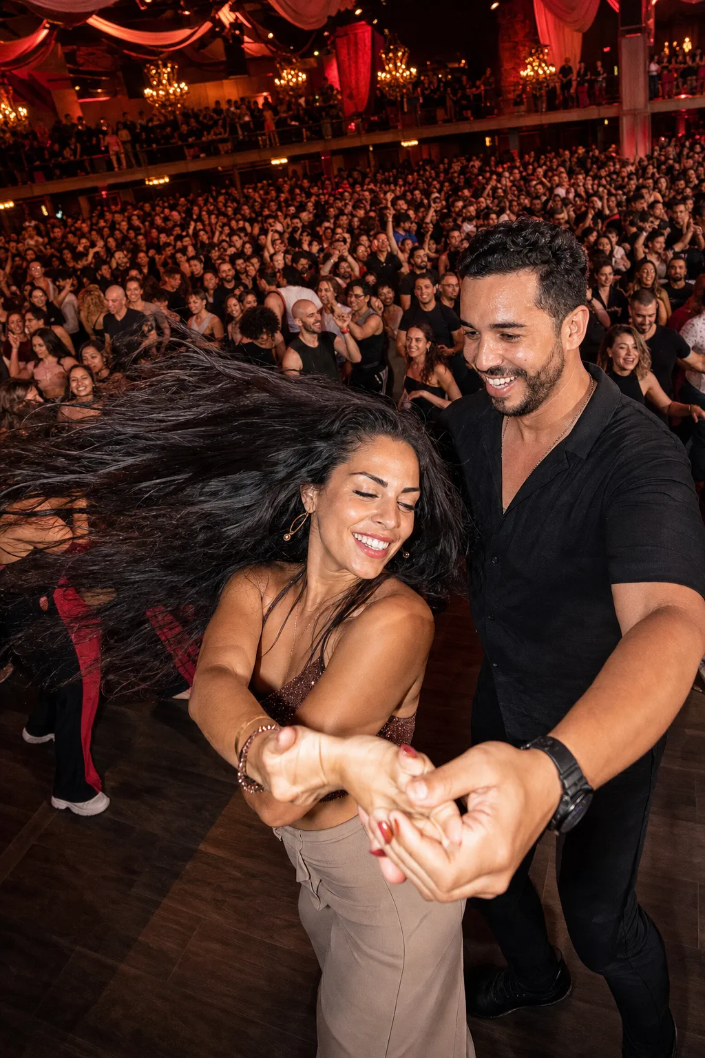 A smiling couple turns together in front of a packed social-dance festival floor.